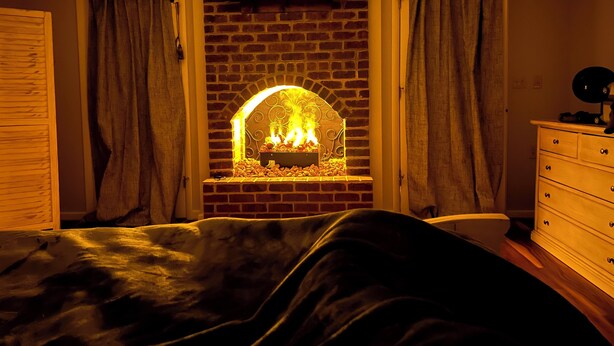 Una habitación con chimenea de ladrillo, un televisor montado encima y un aparador con cajones.