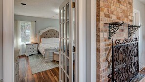 Un dormitorio con cama, mesitas de noche, cómoda, ventana y pared de ladrillo.