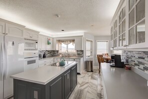 A modern kitchen with white cabinetry, a central island, and a dining area with a table and chairs. - Hilltop Hideaway (Boone)