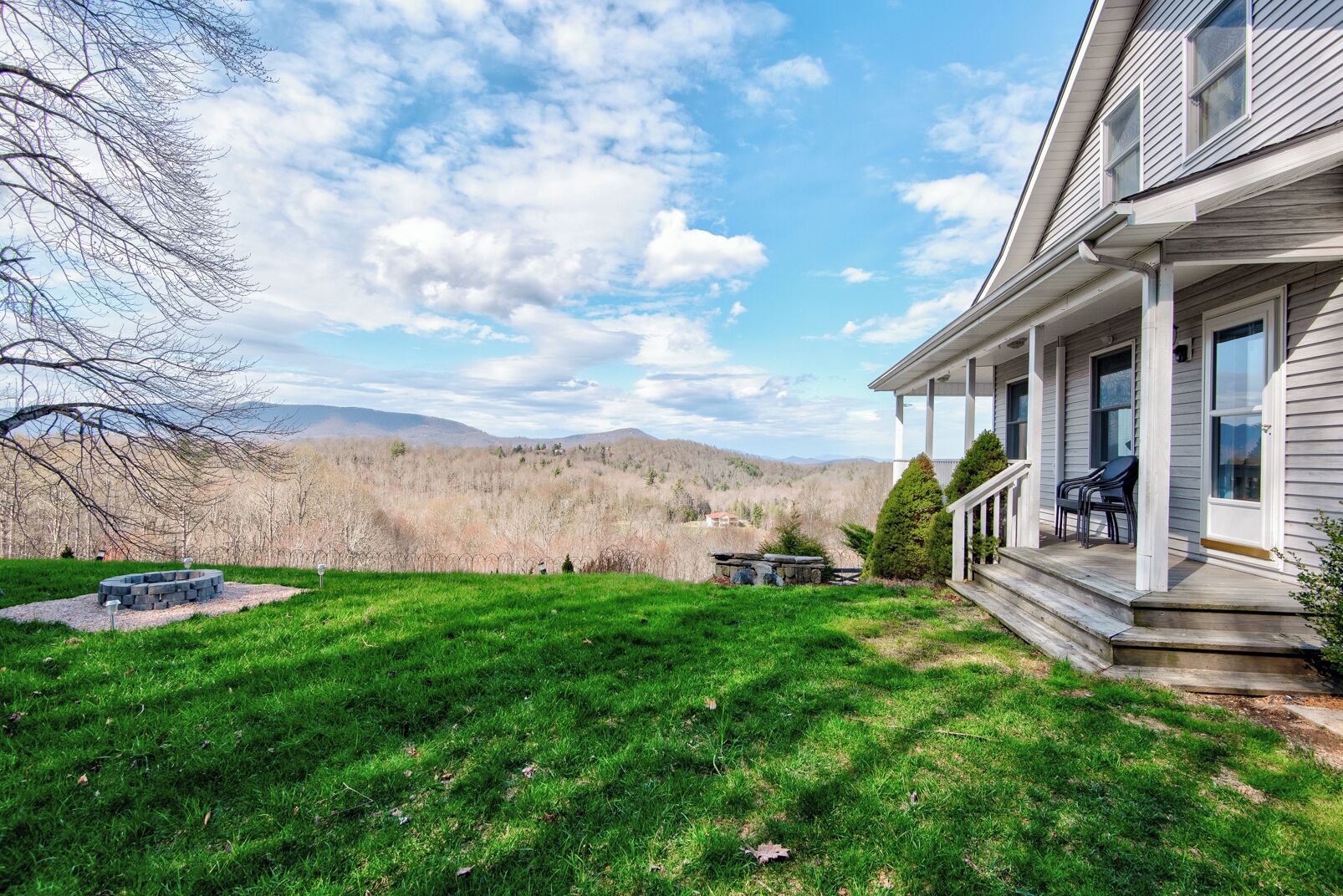 A house with a front porch, a stone fire pit, and a view of a forested mountain range.