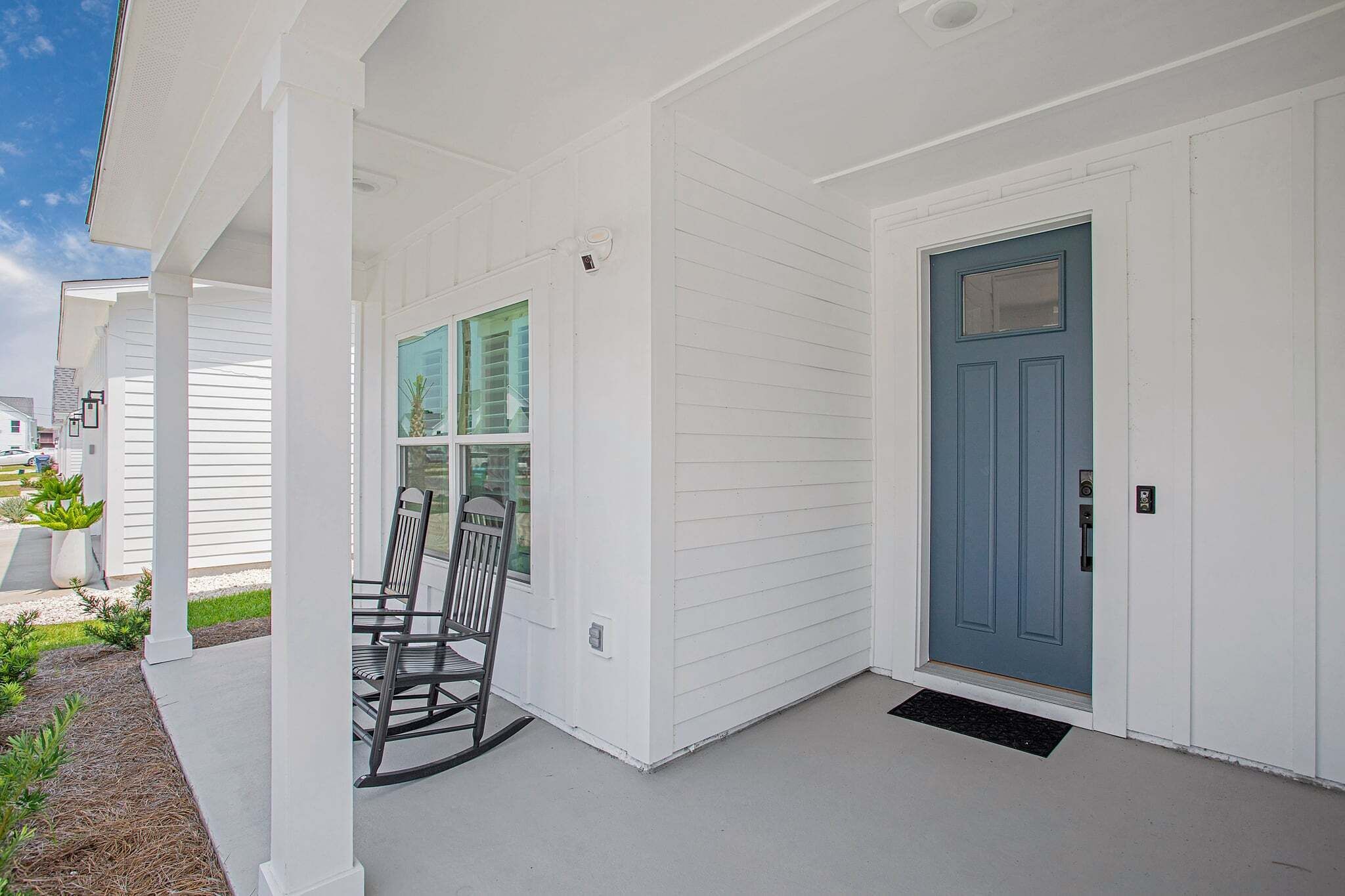 A white building with a blue door, a porch with chairs, and a window with a view.