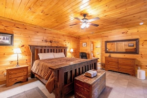 Ein Schlafzimmer einer Holzhütte mit Bett, Schminktisch und Deckenventilator.
