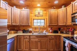 Ein Holzblockhaus-Interieur mit einer Küche, die Holzschränke, eine Edelstahl-Spüle, ein Fenster und eine Mikrowelle zeigt.