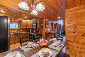 Ein Interieur einer Holzhütte mit einem Esstisch, der für sechs Personen gedeckt ist, Holzschränken, einem Kühlschrank und einer Mikrowelle.