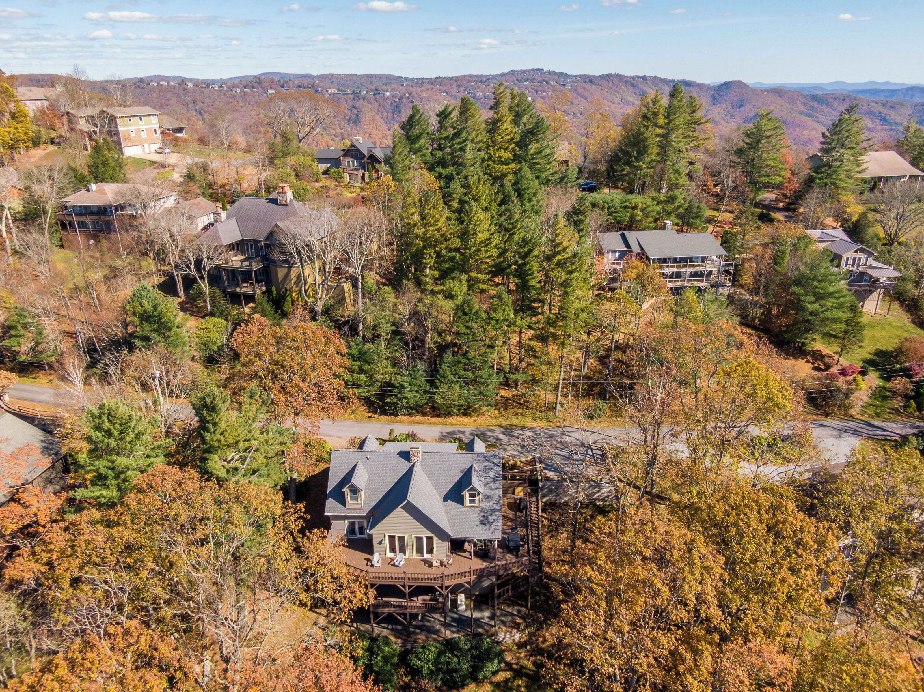 A residential area with houses surrounded by trees and hills in the background.