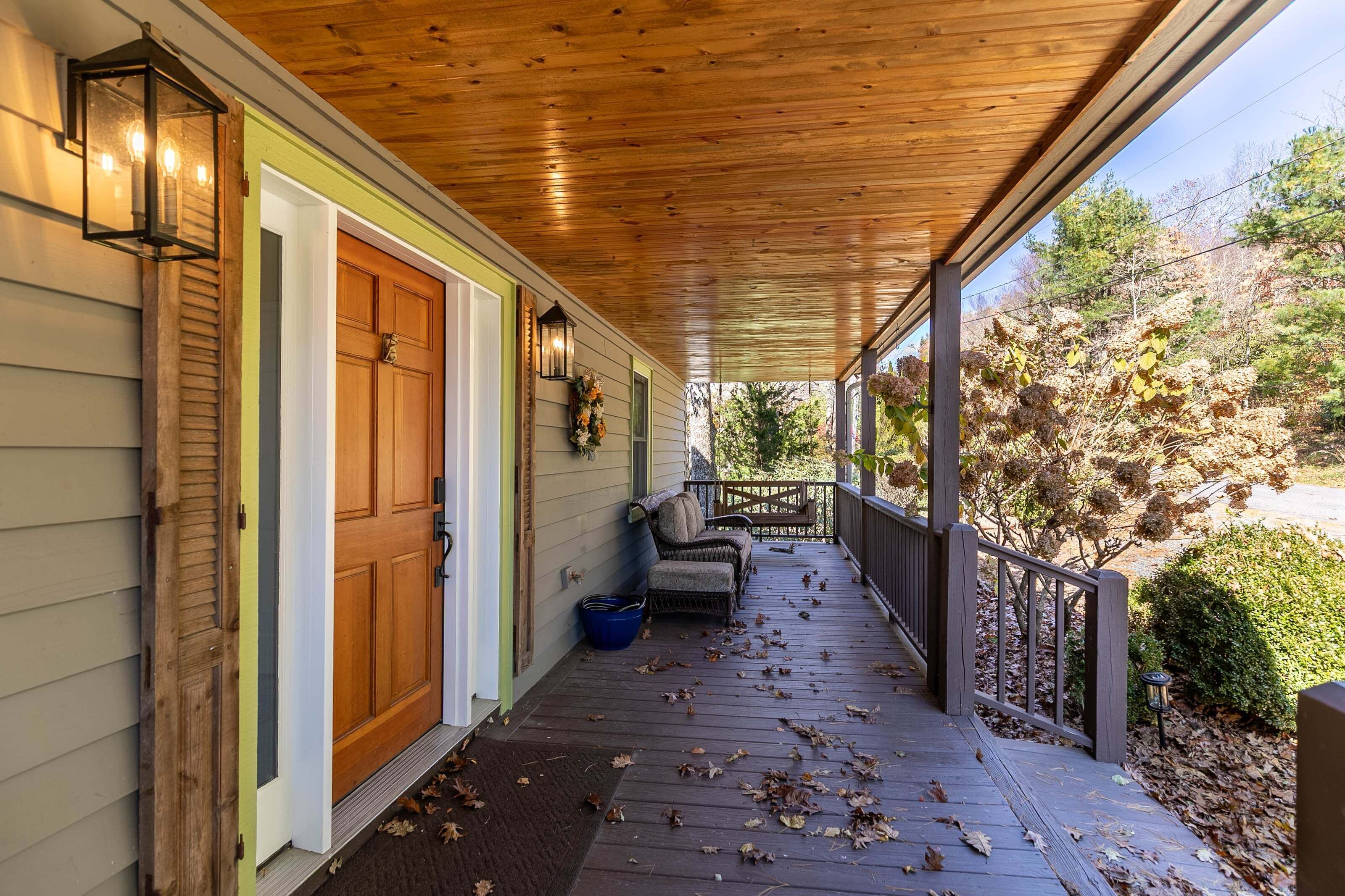 A covered porch with a wooden door, a bench, and a railing.