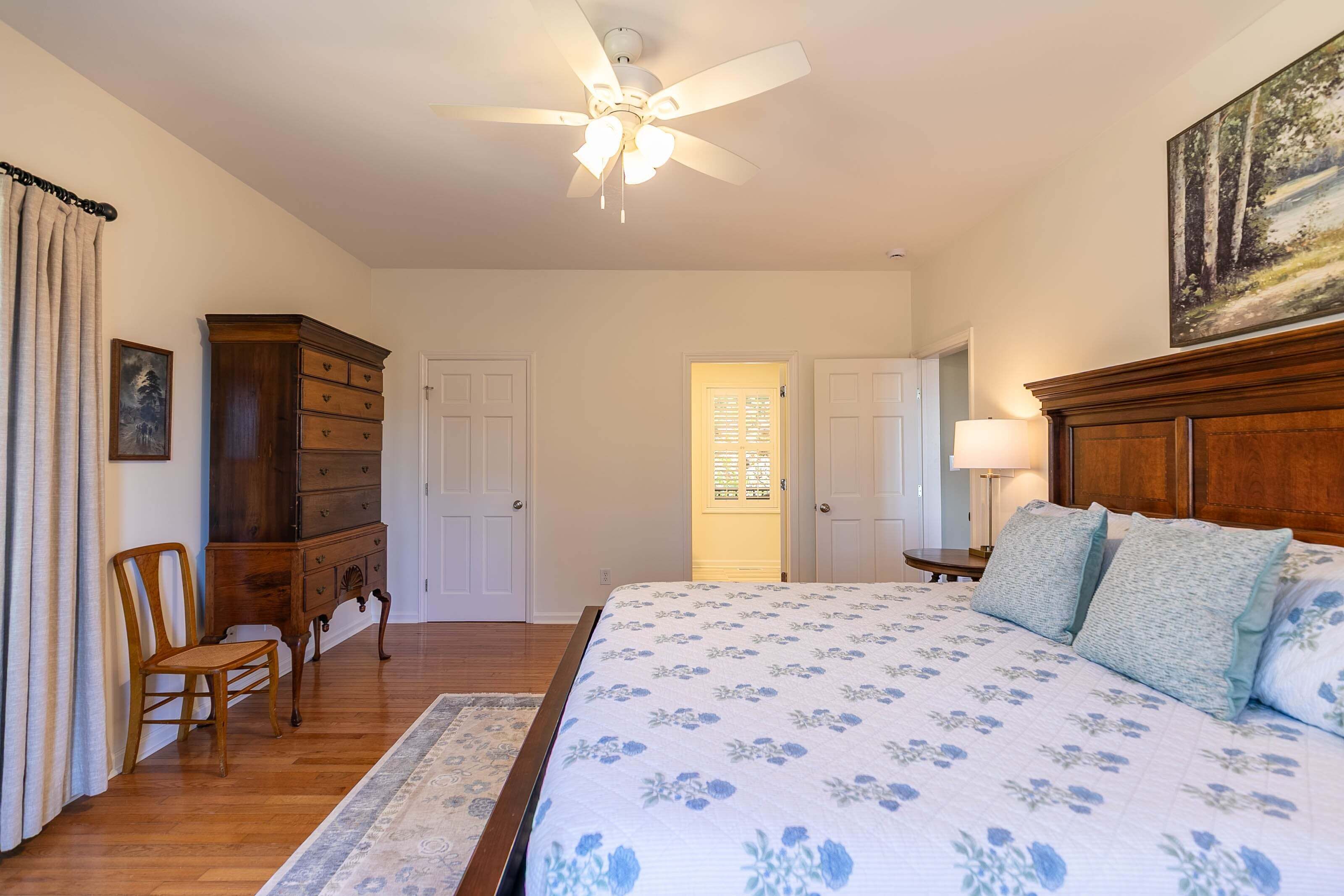 A bedroom with a bed, a ceiling fan, a dresser, a chair, and a painting on the wall.