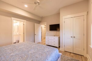 Un dormitorio con cama, cómoda, televisor y dos puertas.