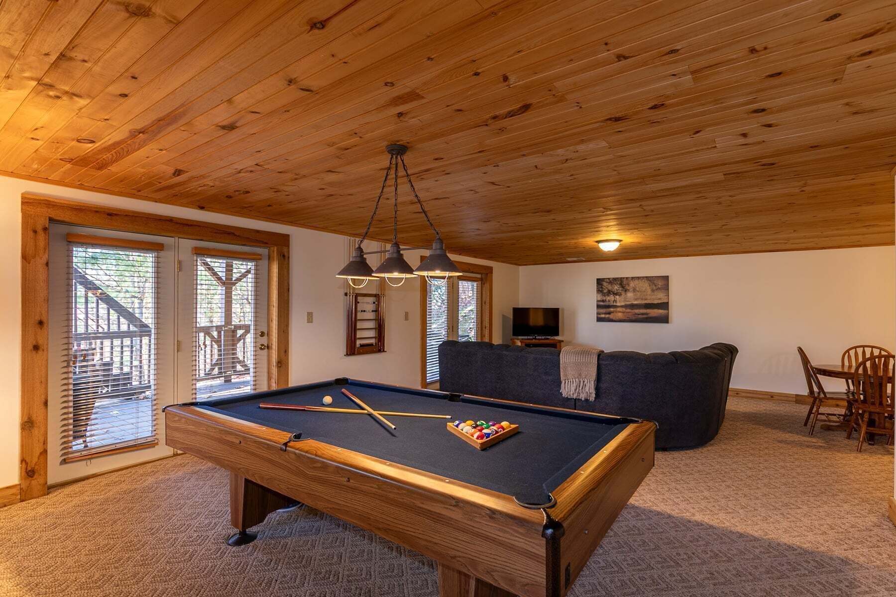 A pool table with balls, a sofa, a TV, and a dining area with chairs.