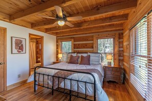 A wooden cabin bedroom with a bed, a ceiling fan, and a window with blinds.