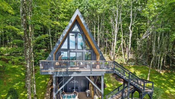 Een moderne chalet met een houten terras, een jacuzzi en een trap naar een balkon.