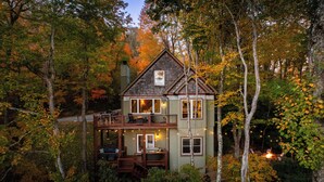 Une cabane à deux étages, entourée d’arbres, avec un balcon et une terrasse.