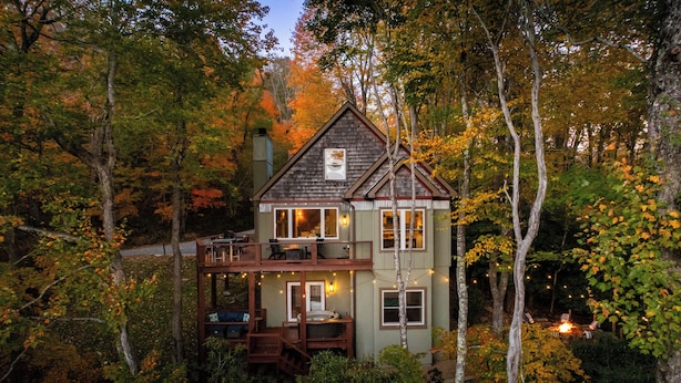 A two-story cabin surrounded by trees with a balcony and deck. - S'more To Love - Pet Friendly, Hot Tub, Pool Table, Views, & More (Banner Elk)