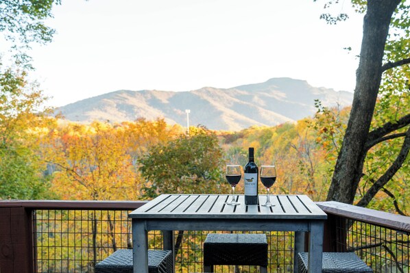 Une table en bois, avec deux verres à vin et une bouteille, placée devant un décor de feuillage automnal et de montagnes.