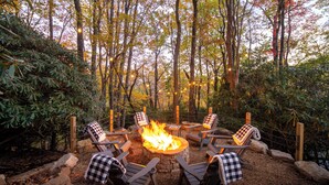 A circular outdoor seating area with a fire pit surrounded by wooden chairs, set in a forested environment. - S'more To Love - Pet Friendly, Hot Tub, Pool Table, Views, & More (Banner Elk)
