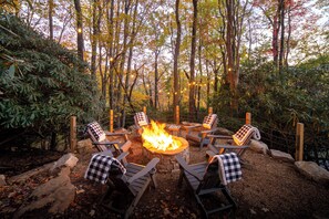 A circular outdoor seating area with a fire pit surrounded by wooden chairs, set in a forested environment. - S'more To Love - Pet Friendly, Hot Tub, Pool Table, Views, & More (Banner Elk)