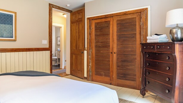 Une chambre à coucher avec un lit, une armoire en bois et une commode sur laquelle est posée une lampe.