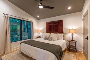 Ein Schlafzimmer mit einem Bett, zwei Nachttischen, einem Deckenventilator, einem Fenster mit Vorhängen und einem Wandteppich.