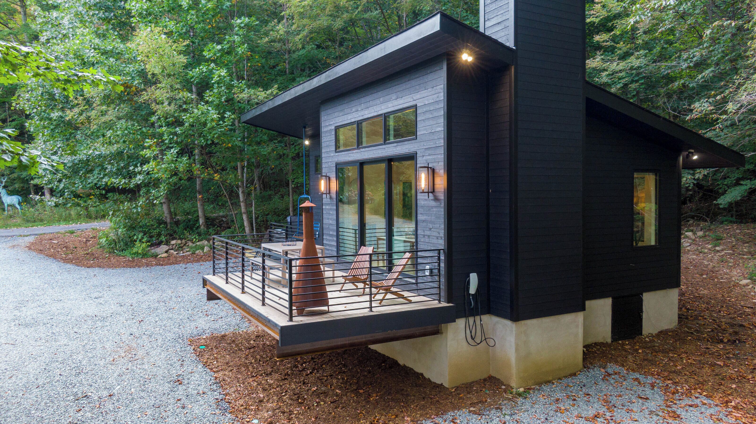 A modern cabin with a deck, large windows, and a stone foundation.