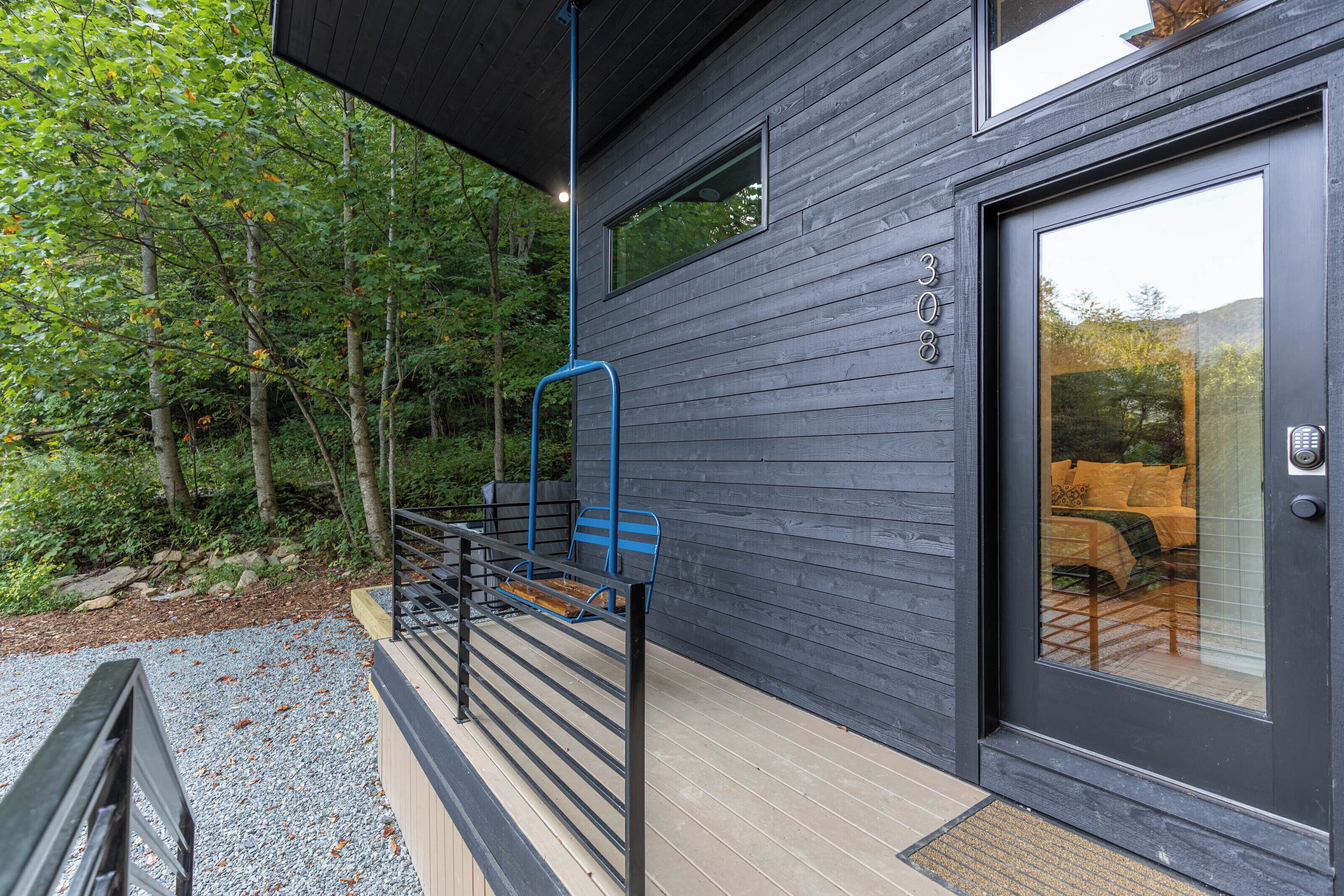 A modern house with a wooden exterior, a glass door, and a small outdoor seating area with a bench and a chair.