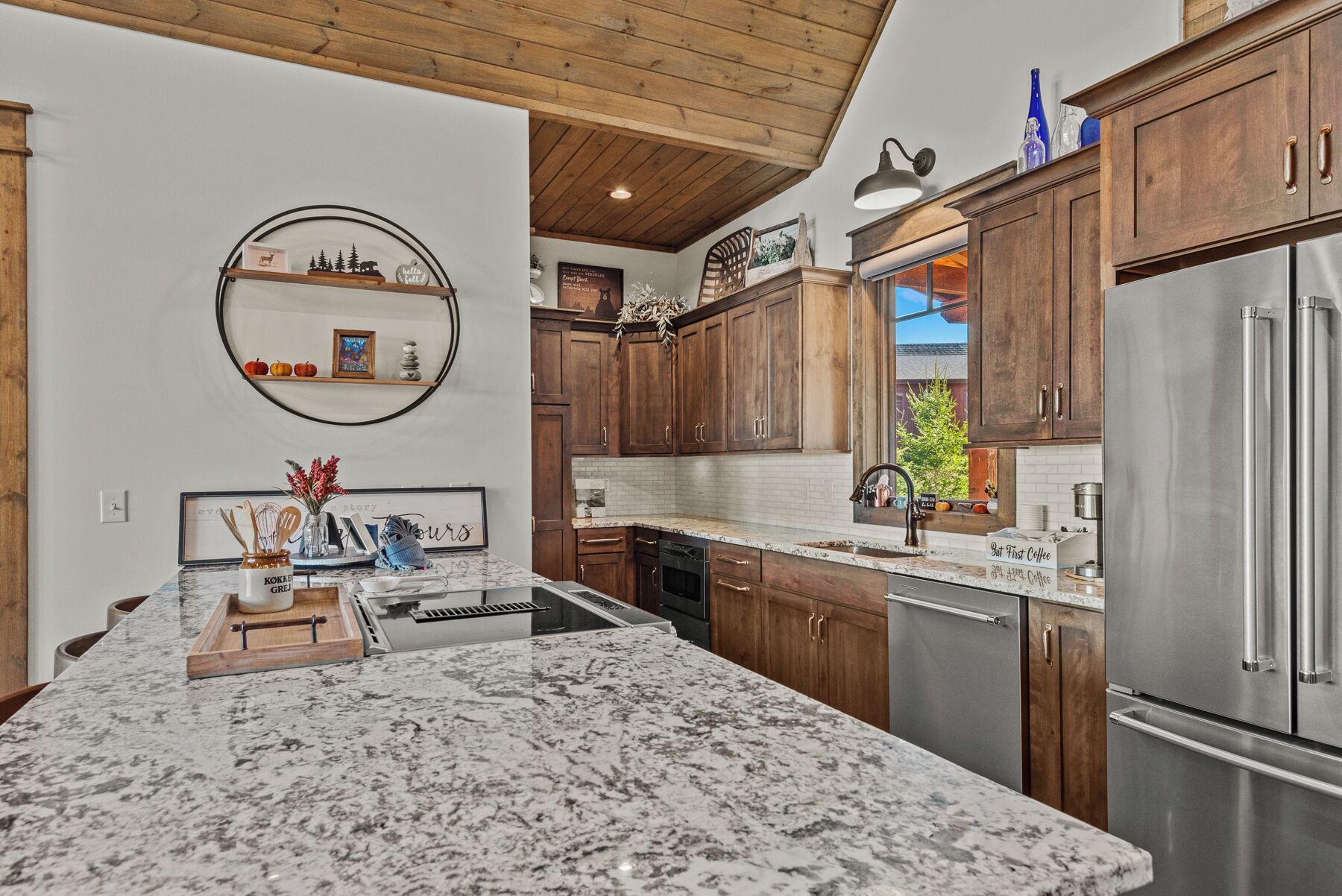 A kitchen with wooden cabinets, a marble countertop, stainless steel appliances, and a hanging light fixture.