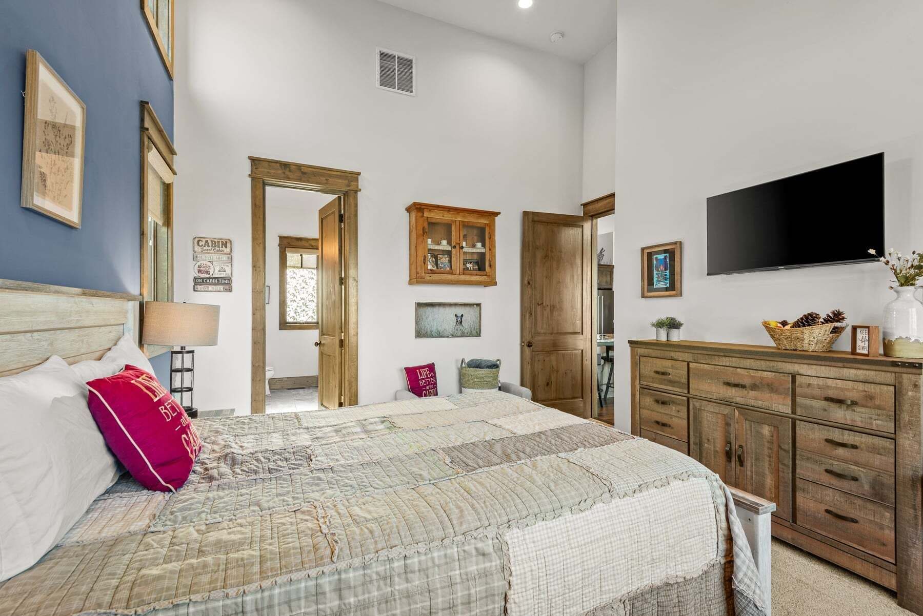 A bedroom with a bed, dresser, television, and a door leading to another room.
