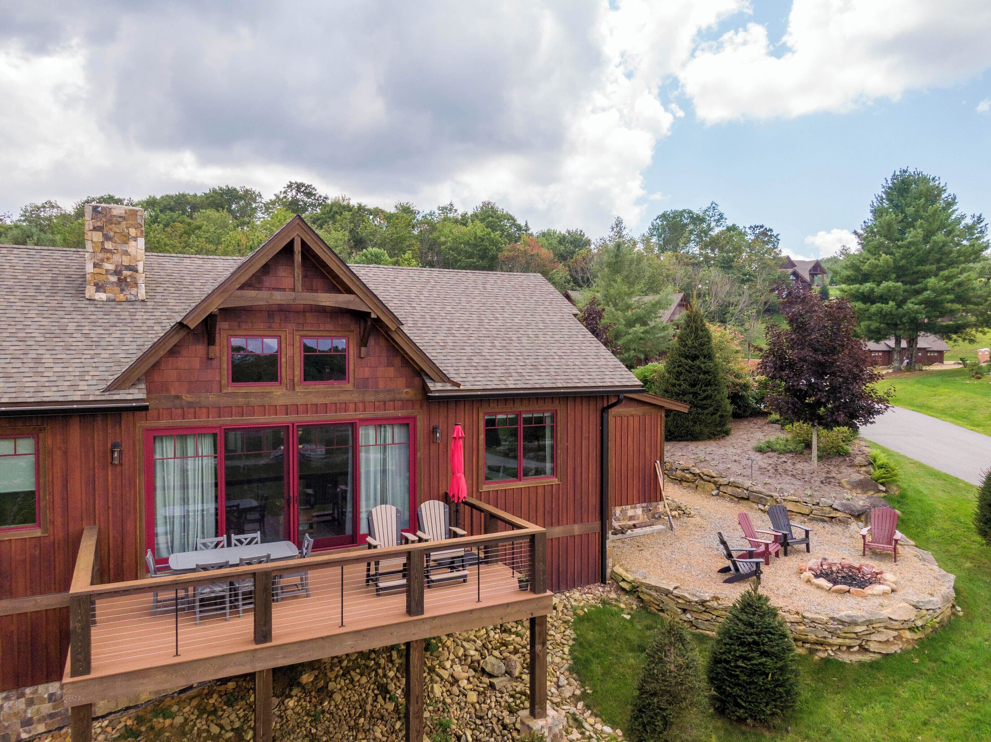 Una cabaña de madera con terraza, ventanas grandes y chimenea de piedra.