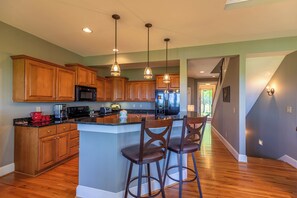 Cocina moderna con armarios de madera, una isla central con taburetes altos y electrodomésticos de acero inoxidable, además de iluminación colgante.