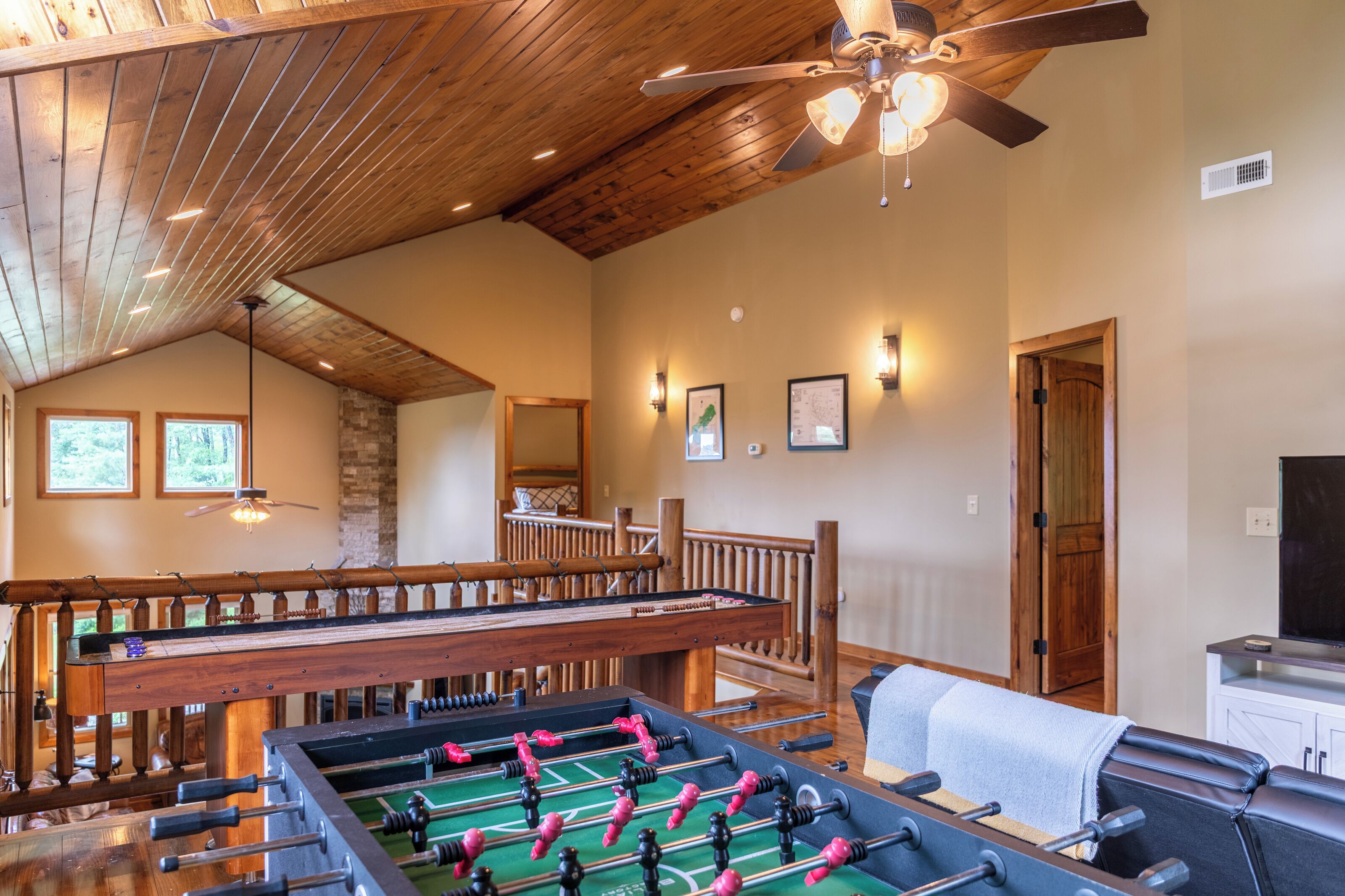 A spacious room with a foosball table, a pool table, and a ceiling fan.