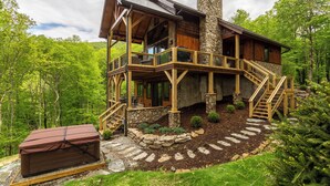 A log cabin with a stone chimney, wooden deck, and a stone staircase leading to the upper level. - Blue Ridge View at Eagles Nest (Banner Elk)