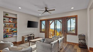 A living room with a television, bookshelves, a coffee table, and a sofa. - Blue Ridge View at Eagles Nest (Banner Elk)