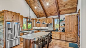 A kitchen with wooden cabinets, stainless steel appliances, and a large island with bar stools. - Blue Ridge View at Eagles Nest (Banner Elk)