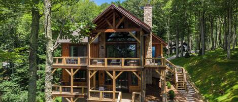 A wooden cabin with a stone chimney, a hot tub, and a deck with outdoor seating.