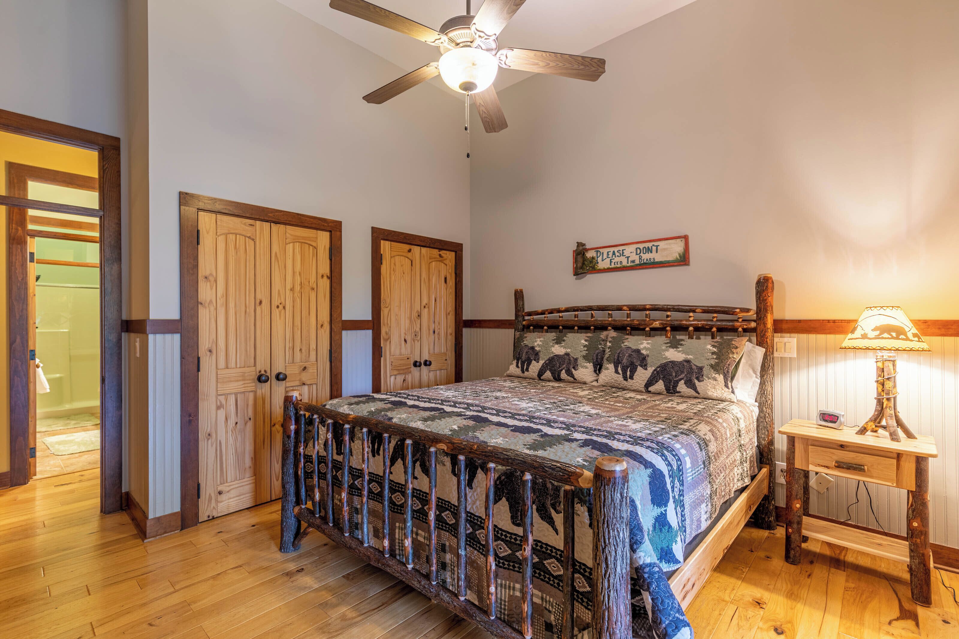 Quarto com cama de madeira, ventoinha no teto e mesa de cabeceira com abajur.