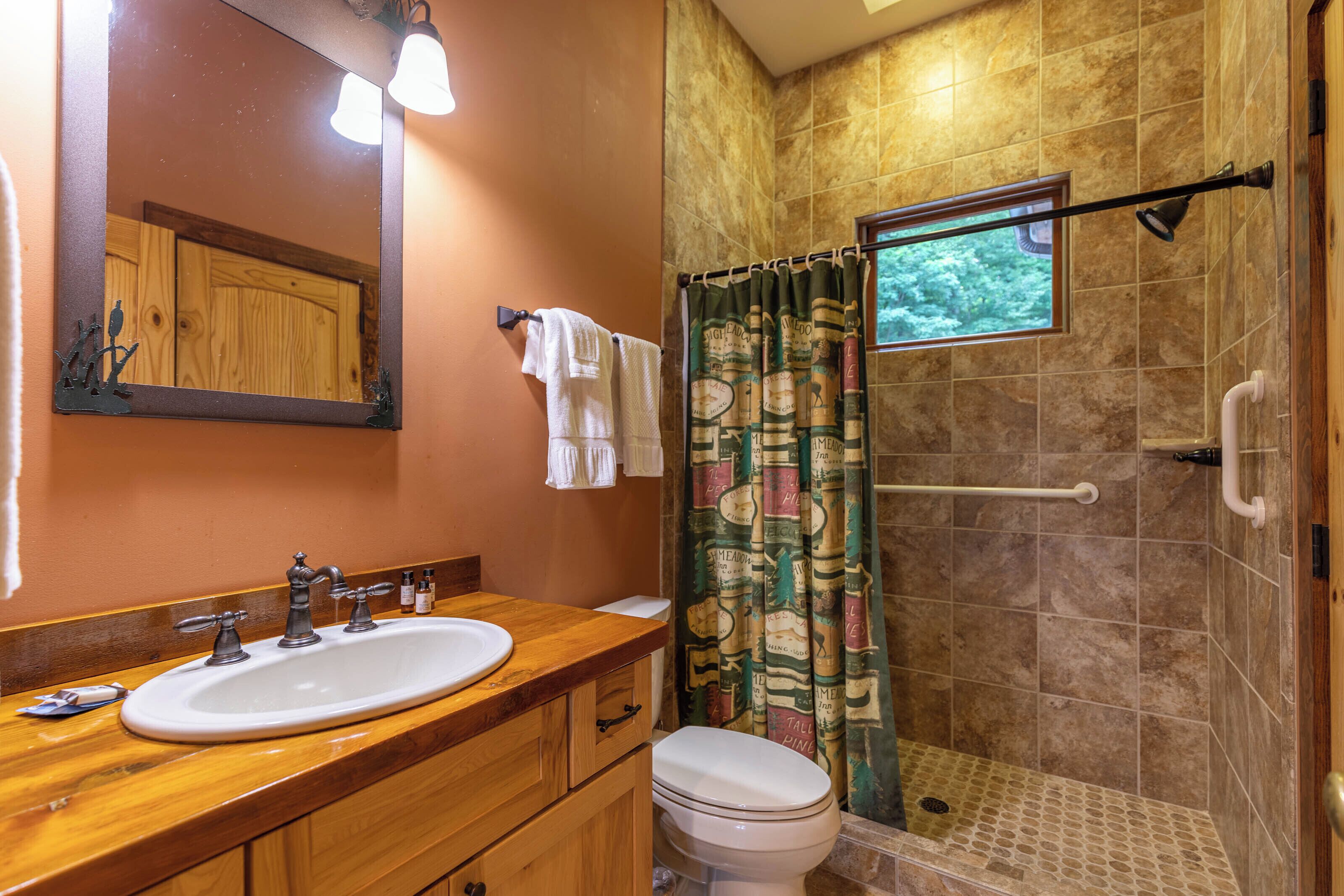 A bathroom with a wooden vanity, a white sink, and a shower with a patterned curtain.