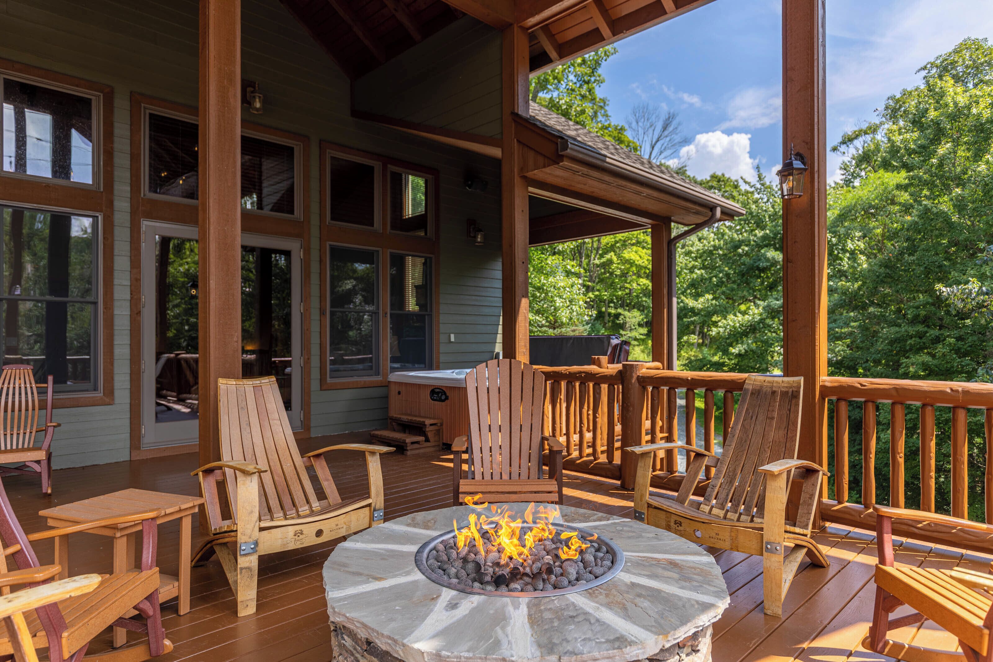 Une terrasse en bois avec des sièges d’extérieur, un foyer en pierre et de grandes fenêtres donnant sur une zone boisée.