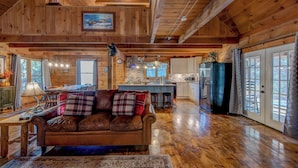A spacious cabin with a wooden interior, a dining area, kitchen, and a cozy living room with a leather sofa. - Hidden Serenity Hot Tub, Fire Pit, Minutes From Boone (Fleetwood)