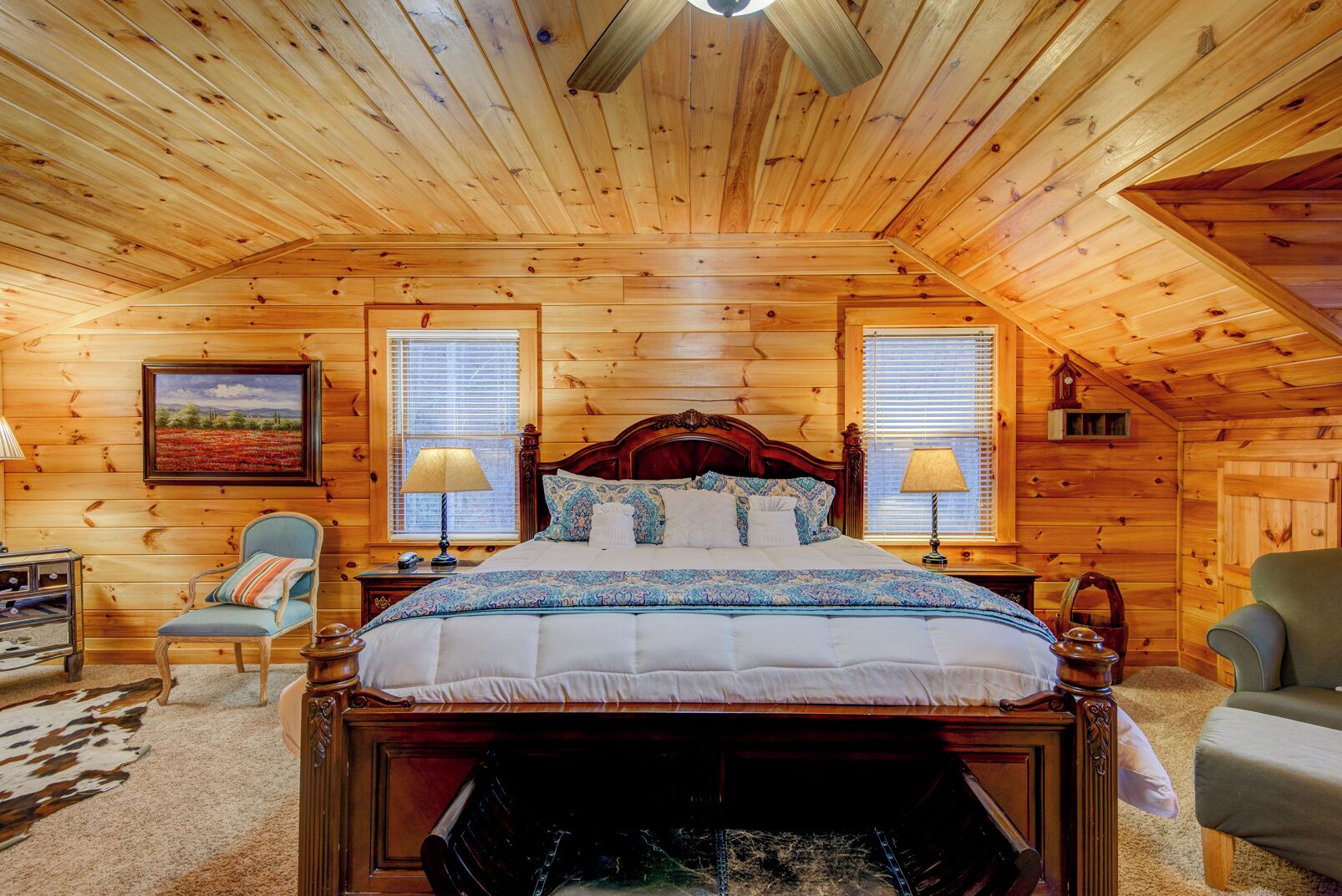 Une chambre confortable dans un chalet en rondins, avec un grand lit, deux fenêtres équipées de stores, un plafond en bois et une décoration rustique.