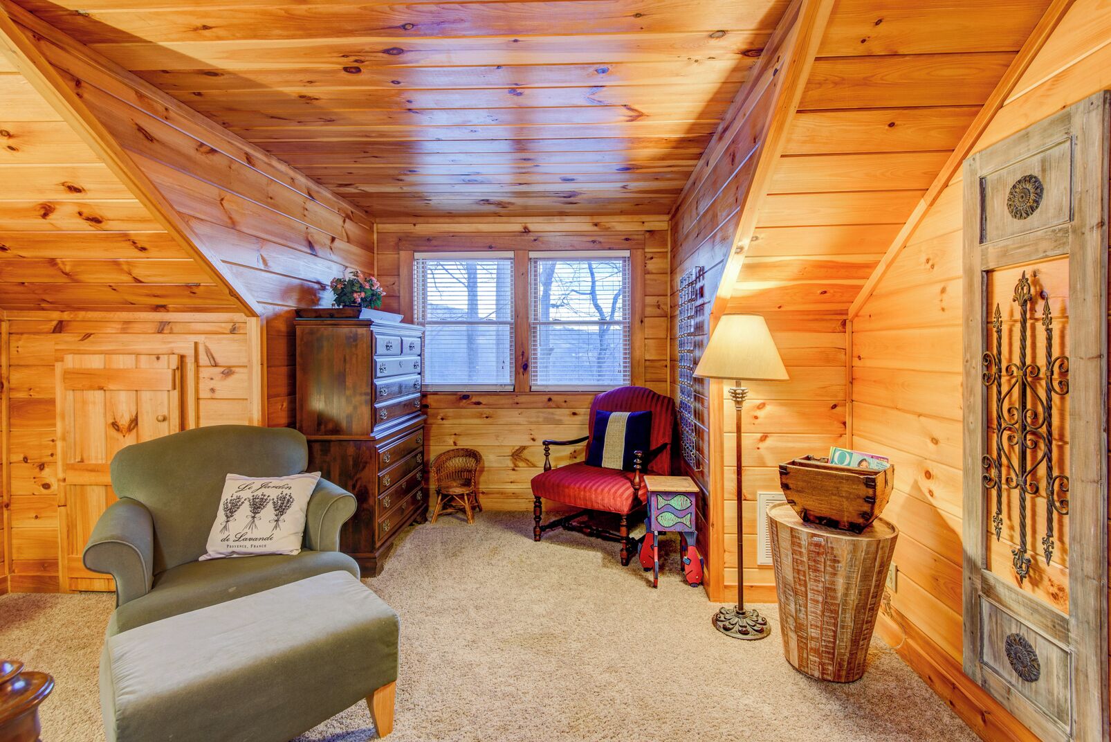 Ein gemütliches Blockhaus-Interieur mit Holzwänden, einem Fenster, einer Lampe, einem Sessel, einer Kommode und einem kleinen Tisch.