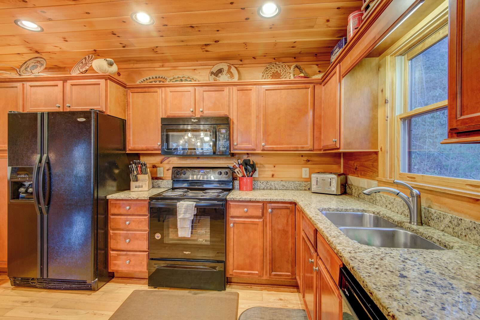 A kitchen with wooden cabinets, a stainless steel refrigerator, a microwave, a stove, and a sink.