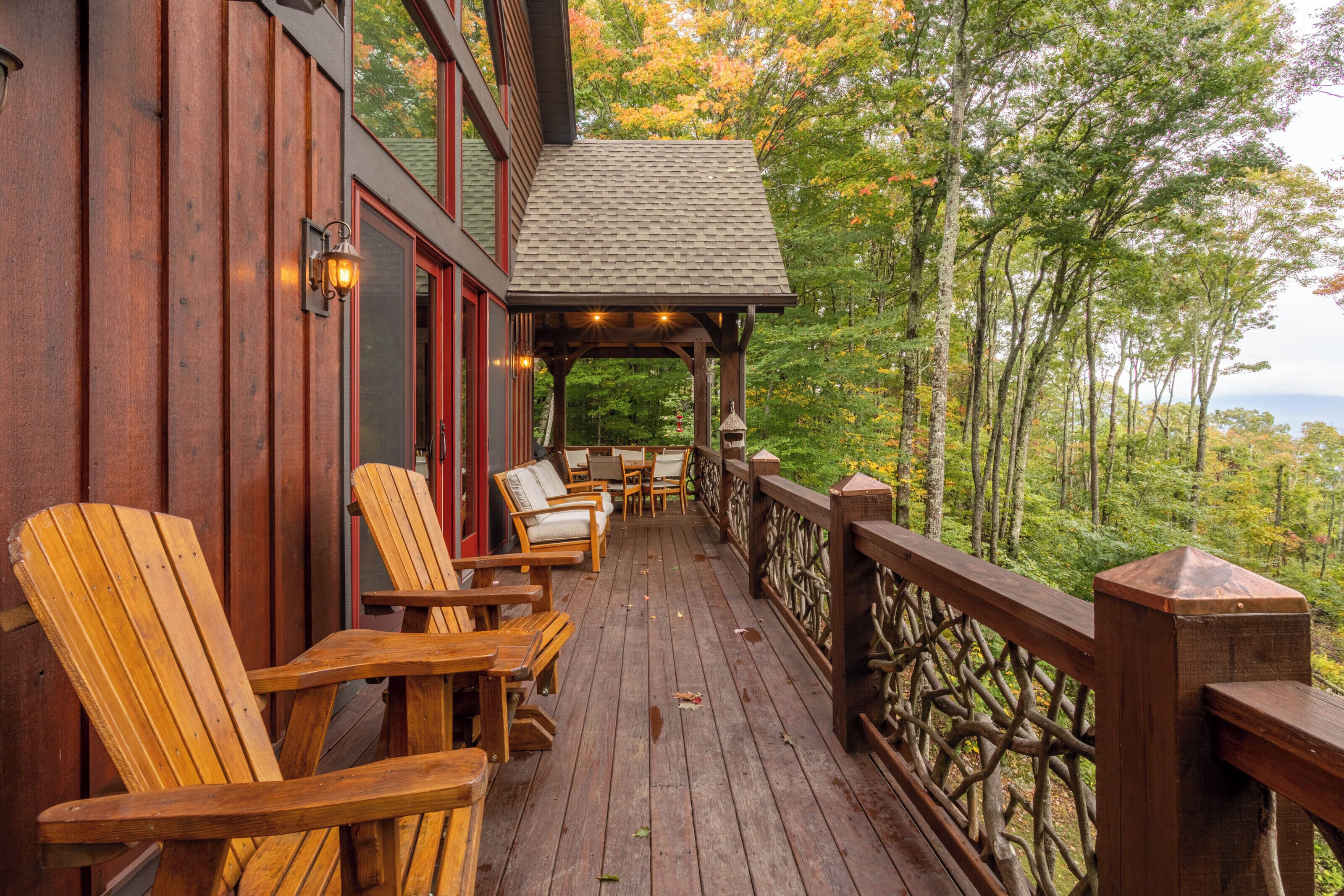 Una terraza de madera con sillas Adirondack y un área de estar cubierta con vistas a un paisaje boscoso.