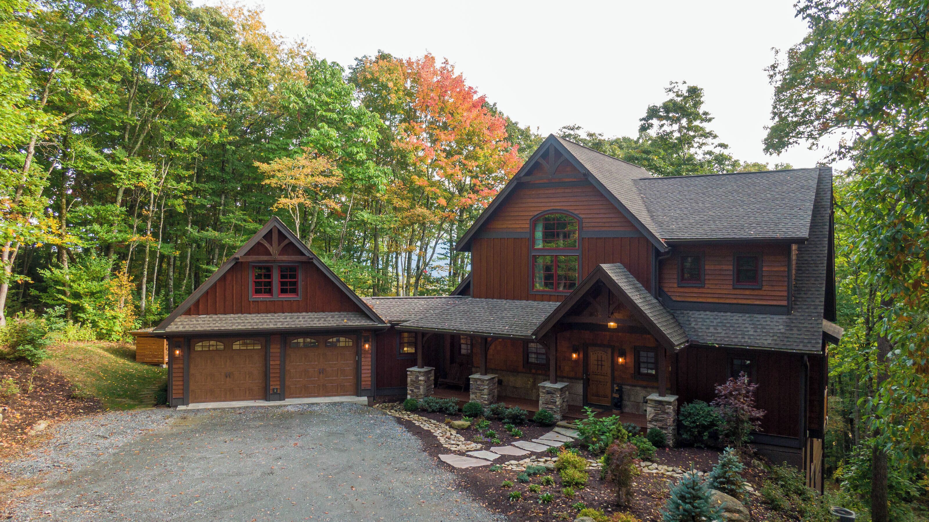 A large, two-story log cabin with a garage, surrounded by a forest.