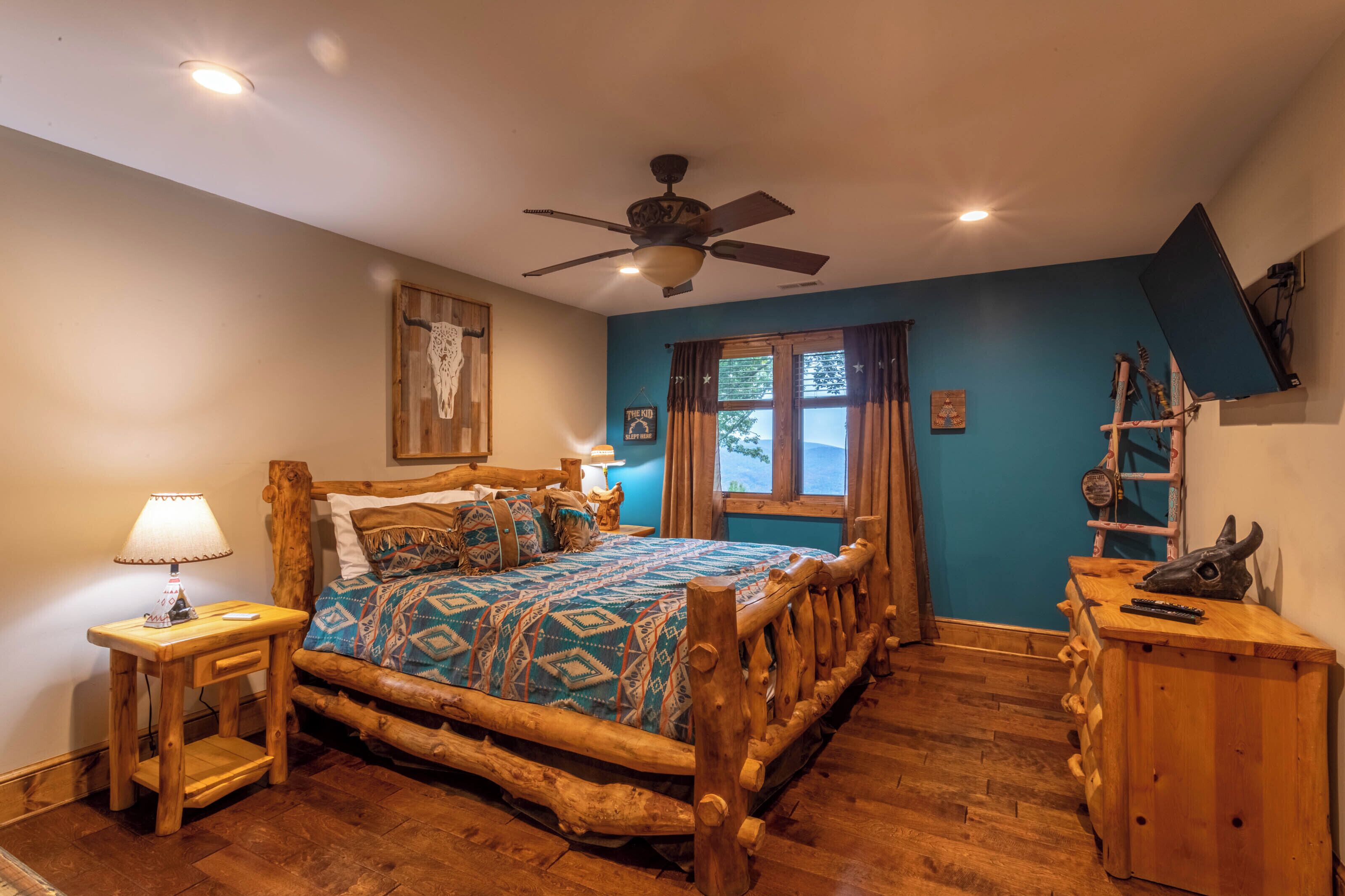 A rustic bedroom with a wooden bed, a ceiling fan, a nightstand with a lamp, and a wooden dresser.