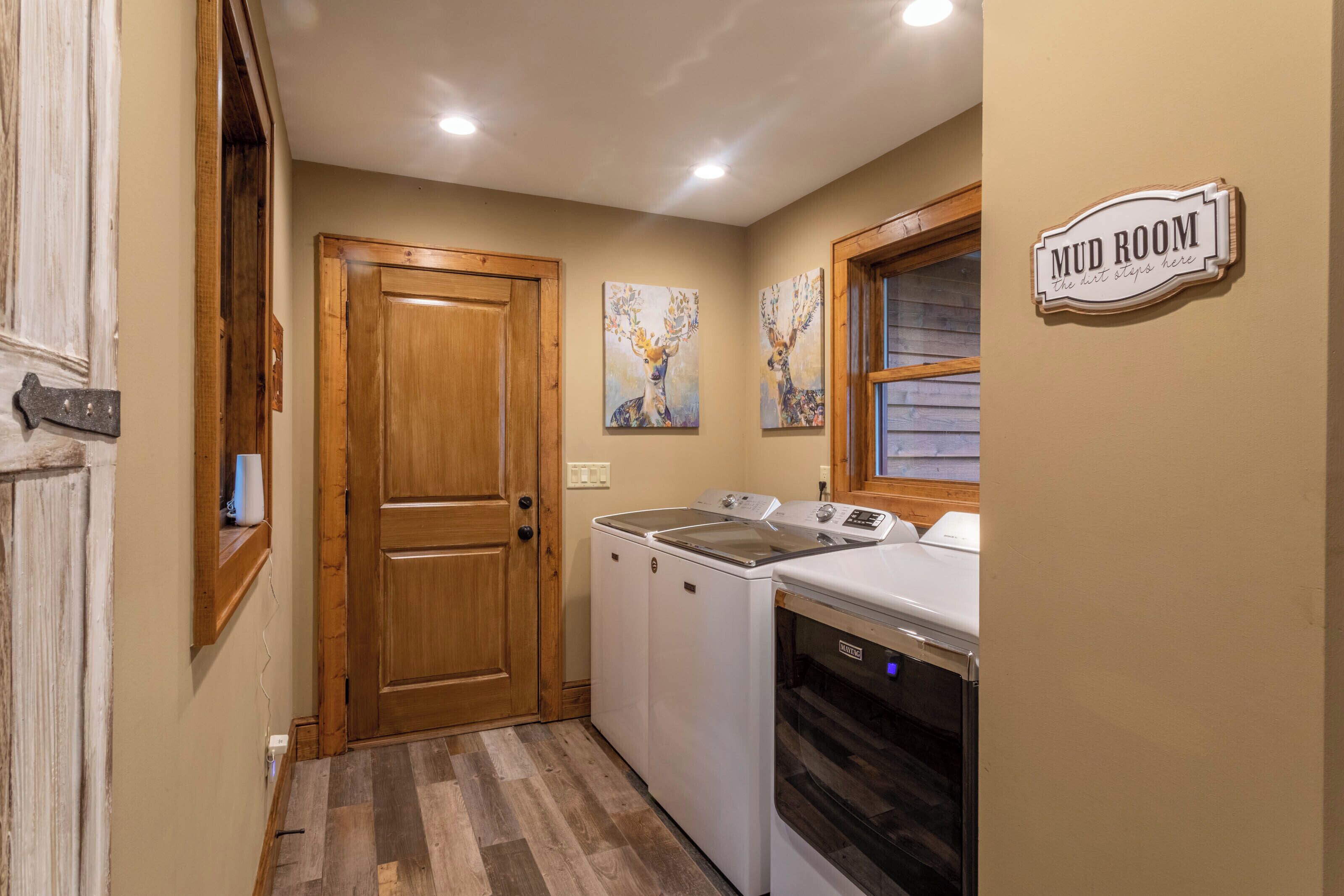 A laundry room with wooden doors, a washing machine, a dryer, and two wall-mounted paintings.