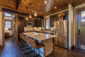 A kitchen with wooden ceiling, stainless steel appliances, and a central island with bar stools. - 2 Bears Retreat at Eagles Nest (Banner Elk)
