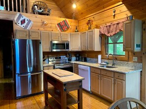 A wooden cabin-style kitchen with a stainless steel refrigerator, microwave, stove, and dishwasher. - Baird's Creek Cabin (Vilas)