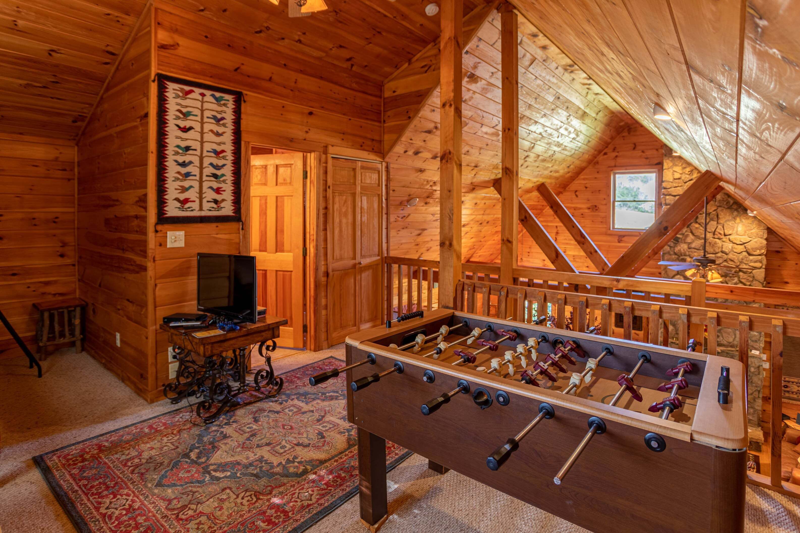 A wooden interior with a foosball table, a television, and a staircase leading to an upper level.