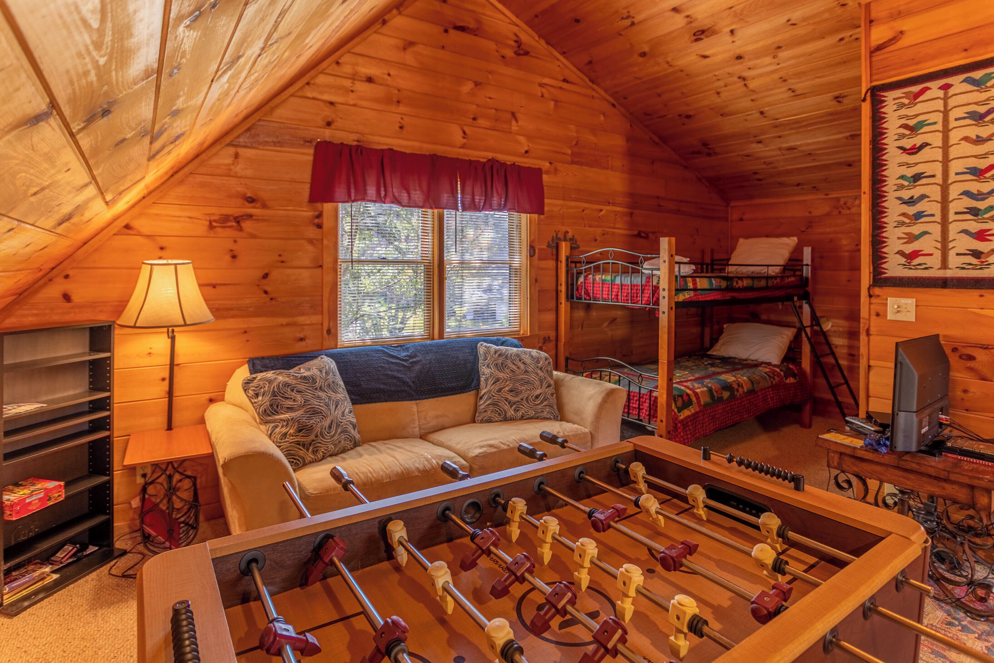 Une pièce chaleureuse dans un chalet en bois, avec un canapé, une table de baby-foot, un lit superposé et une lampe.