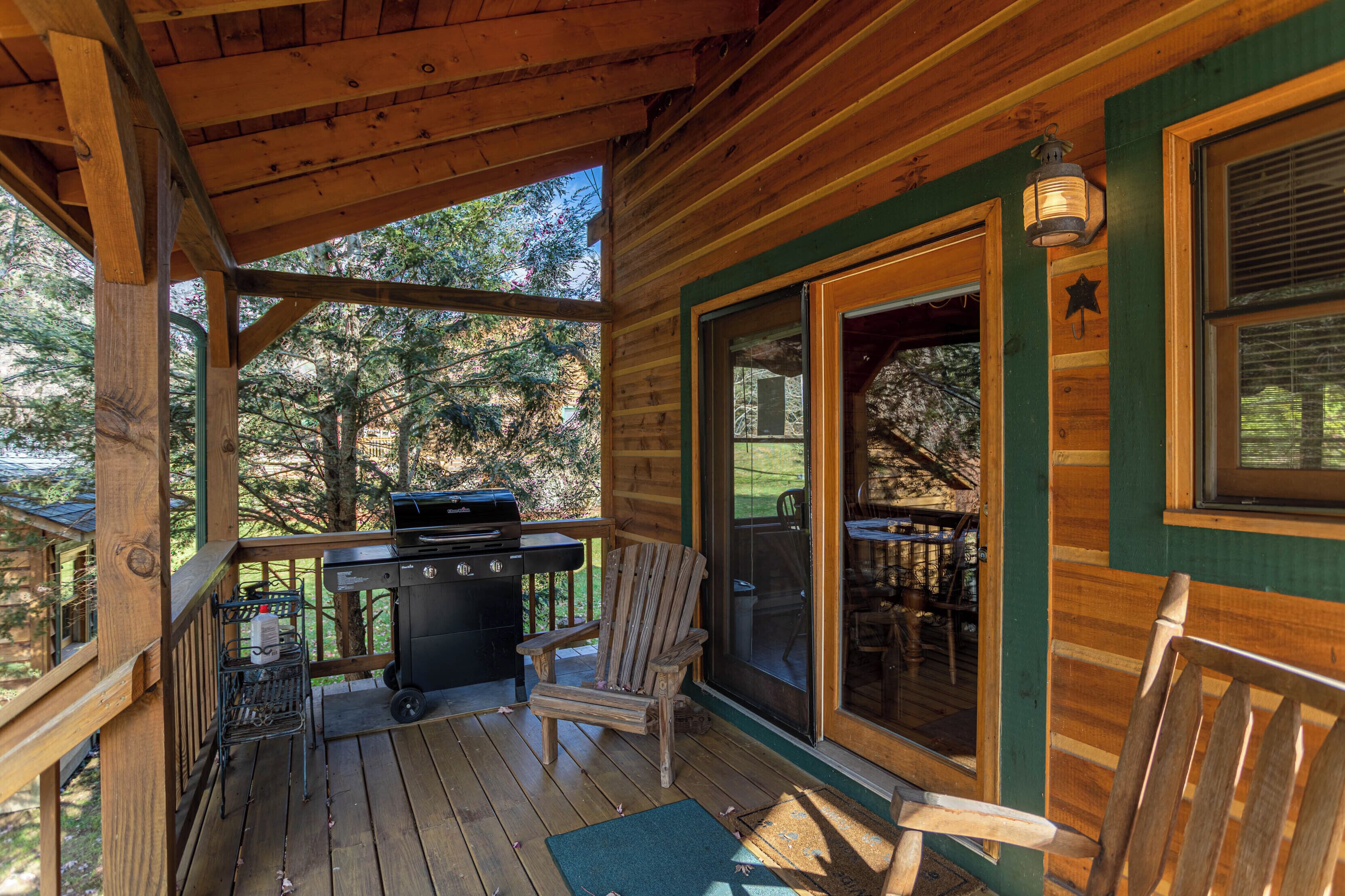A wooden deck with a grill, chairs, and a view of the surrounding trees.