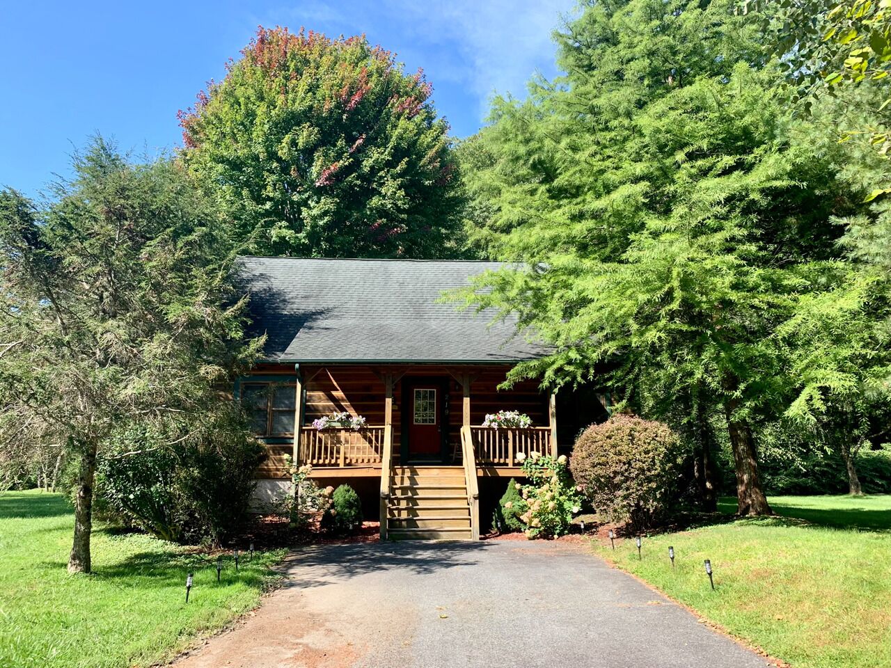 A log cabin with a front porch, surrounded by trees and a gravel path.